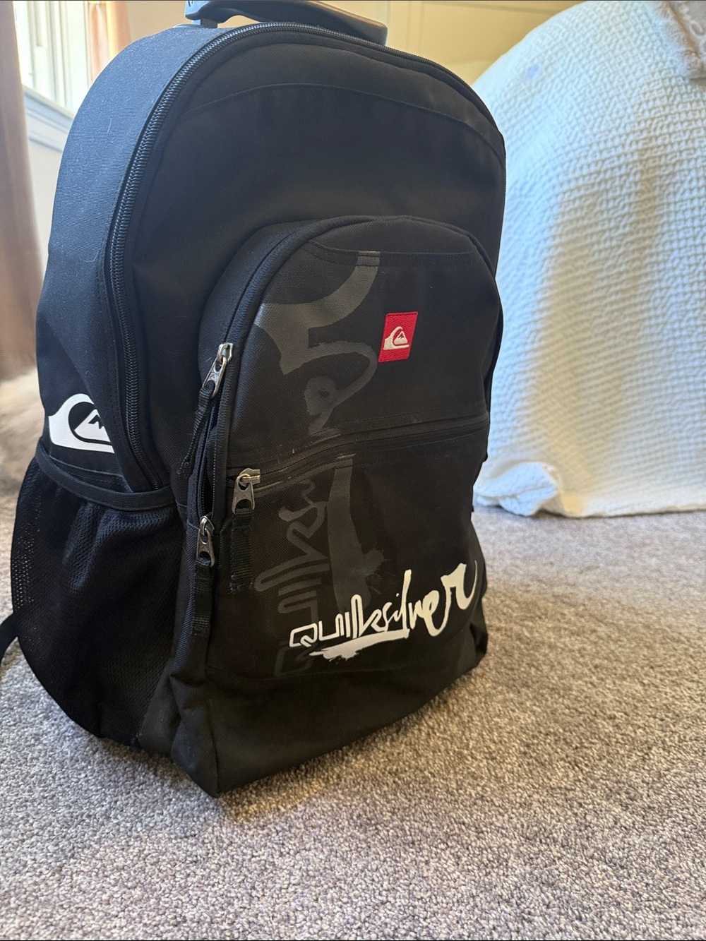 Quicksilver  Black Backpack / luggage  
on wheels with White Logo and Red Patch